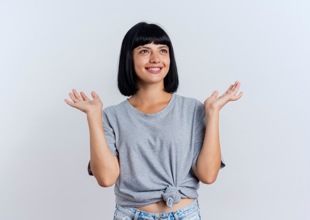 Sonriente joven morena mujer caucásica se encuentra con las manos levantadas mirando al lado