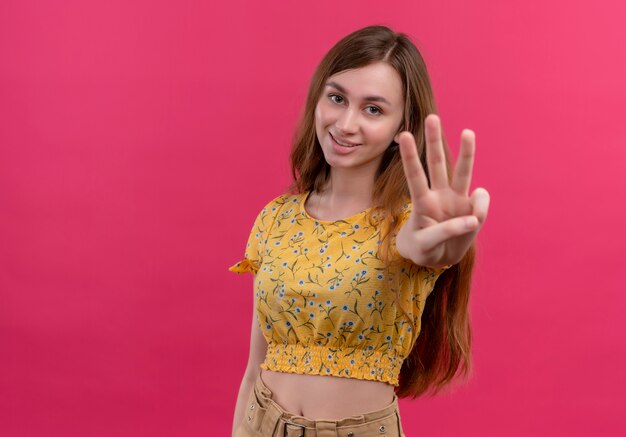 Sonriente joven mostrando tres en la pared rosa aislada con espacio de copia