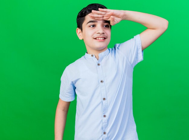 Sonriente joven muchacho caucásico mirando al lado en la distancia aislado en la pared verde con espacio de copia