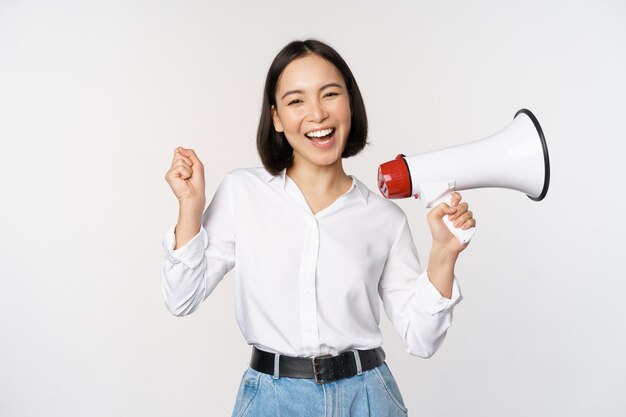 Sonriente joven mujer asiática posando con megáfono concepto de anuncio de noticias e información de pie sobre fondo blanco.