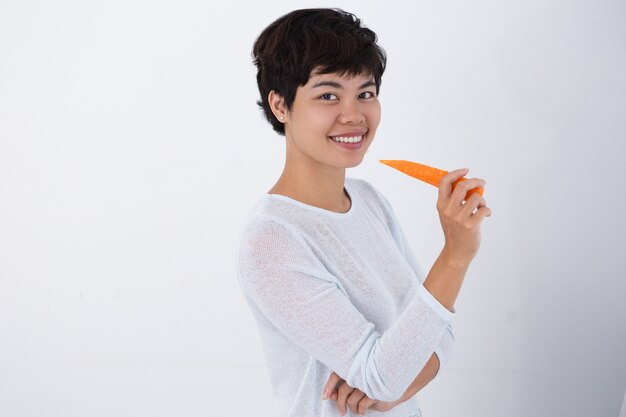 Sonriente joven mujer asiática sosteniendo zanahoria
