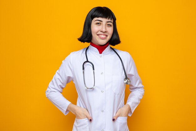 Sonriente joven mujer bastante caucásica en uniforme médico con estetoscopio mirando