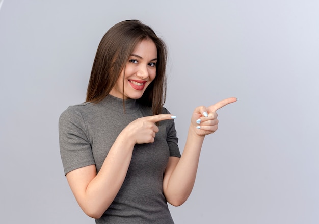 Foto gratuita sonriente joven mujer bonita apuntando al lado aislado sobre fondo blanco con espacio de copia