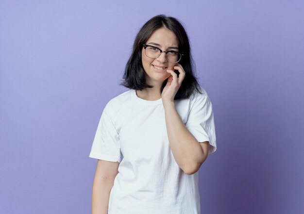 Sonriente joven mujer bonita con gafas poniendo la mano en la mejilla