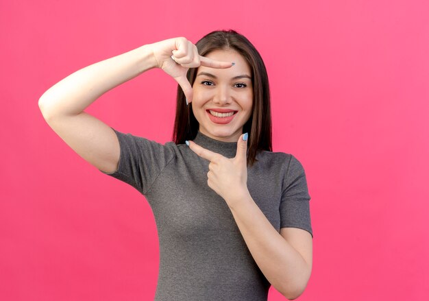 Sonriente joven mujer bonita haciendo gesto de marco aislado sobre fondo rosa con espacio de copia