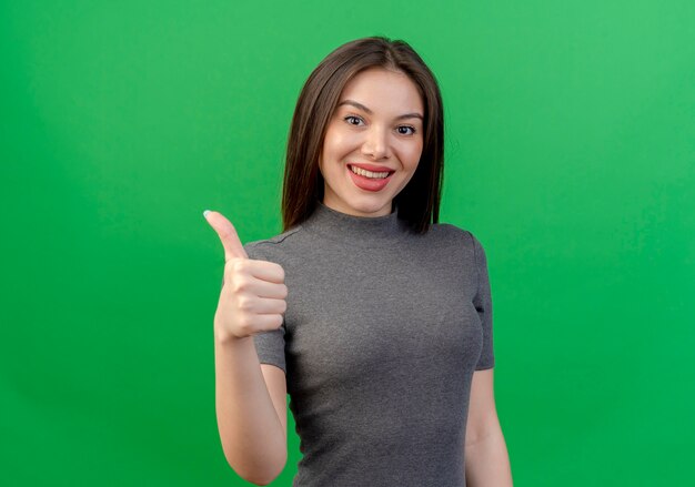 Sonriente joven mujer bonita mostrando el pulgar hacia arriba aislado sobre fondo verde con espacio de copia