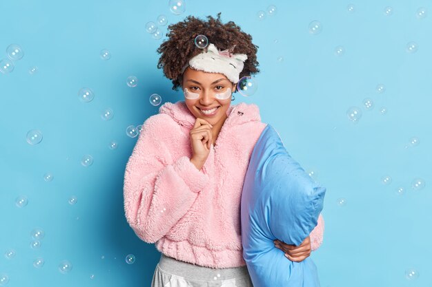 Foto gratuita sonriente joven mujer bonita de piel oscura suave con cabello afro tiene barbilla mira directamente a la cámara