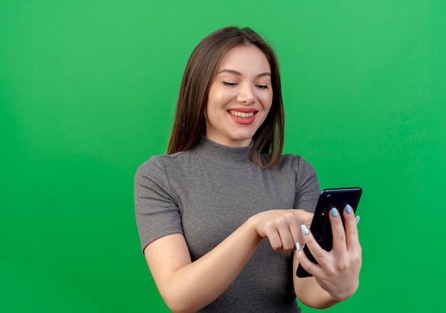 Sonriente joven mujer bonita mediante teléfono móvil aislado sobre fondo verde con espacio de copia