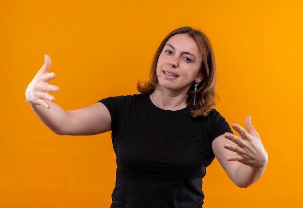 Sonriente joven mujer casual con los brazos abiertos en el espacio naranja aislado