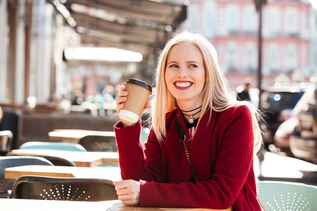 Sonriente joven mujer caucásica sentado en la cafetería al aire libre