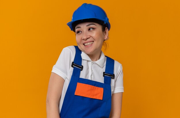 Sonriente joven mujer constructora asiática con casco de seguridad azul mirando al lado