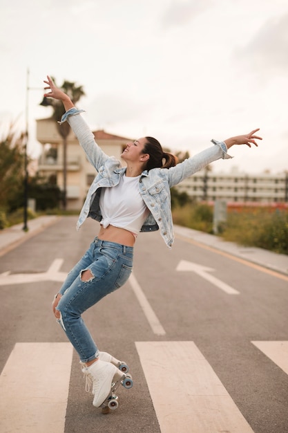 Sonriente joven mujer patinadora bailando con patín en el camino