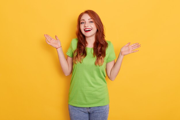 Sonriente joven mujer pelirroja en ropa casual, posando aislado, extendiendo las manos a un lado