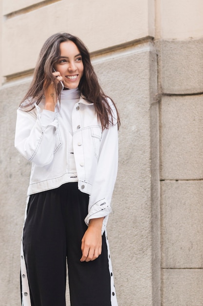 Sonriente joven mujer de pie fuera hablando por teléfono móvil