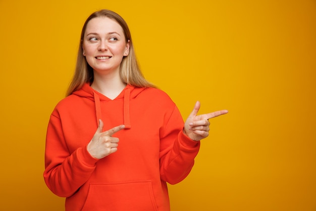 Sonriente joven mujer rubia mirando y apuntando al lado