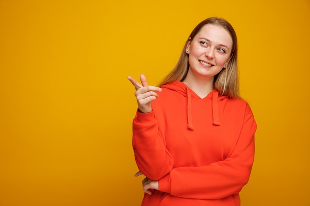 Sonriente joven mujer rubia mirando y apuntando al lado