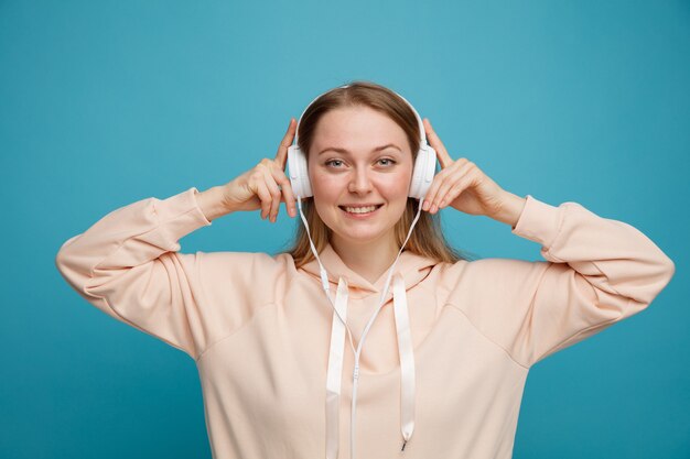 Sonriente joven mujer rubia vistiendo y agarrando auriculares escuchando música