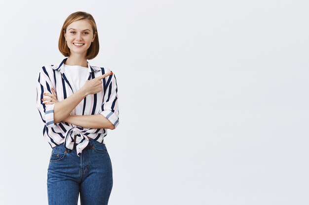 Sonriente joven mujer segura apuntando hacia la esquina superior derecha en copyspace