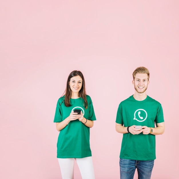 Sonriente joven y mujer sosteniendo teléfono móvil contra el fondo rosa