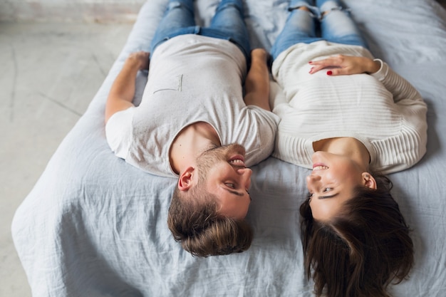 Sonriente joven pareja acostada en la cama en casa en traje casual, hombre y mujer pasando tiempo feliz juntos, relajante, amor y romance