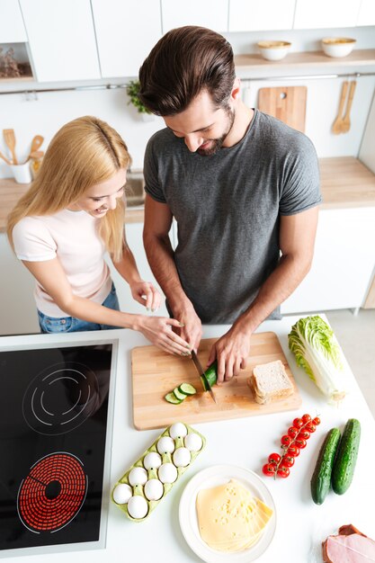 Sonriente joven pareja amorosa de pie en la cocina y cocinar