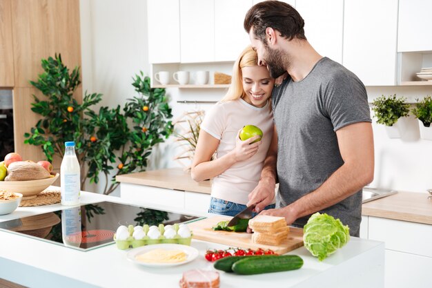 Sonriente joven pareja amorosa de pie en la cocina y cocinar