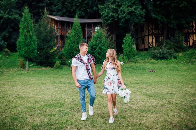 Sonriente joven pareja caminando por el campo con flores en el parque de verano.