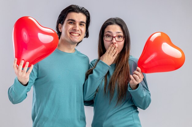 Sonriente joven pareja en el día de San Valentín sosteniendo globos de corazón aislado sobre fondo blanco.