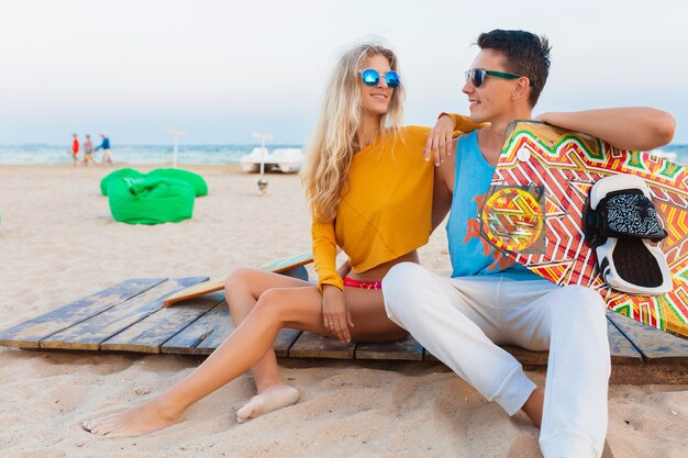 Sonriente joven pareja divirtiéndose en la playa con tabla de kitesurf en vacaciones de verano