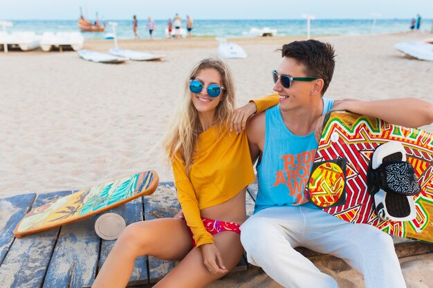 Sonriente joven pareja divirtiéndose en la playa con tabla de kitesurf en vacaciones de verano