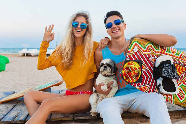 Sonriente joven pareja divirtiéndose en la playa con tabla de kitesurf en vacaciones de verano