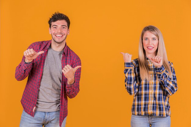 Sonriente joven pareja haciendo gesto de pulgar a la otra contra un fondo naranja