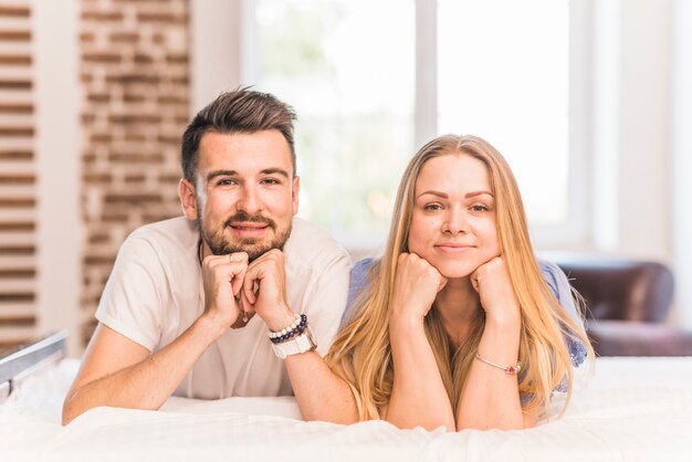 Sonriente joven pareja inclinada la cabeza en la mano acostado en la cama