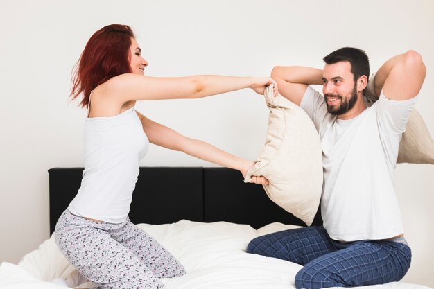 Sonriente joven pareja jugando con almohadas en la cama