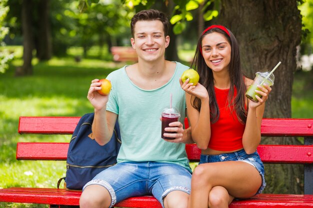 Sonriente joven pareja con manzanas y batidos