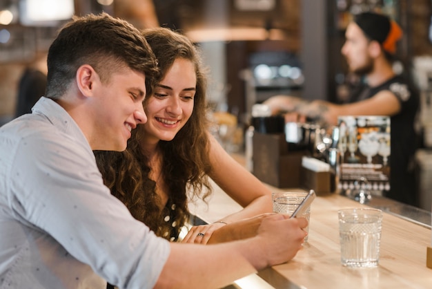 Foto gratuita sonriente joven pareja mirando el teléfono móvil cerca de la barra de bar