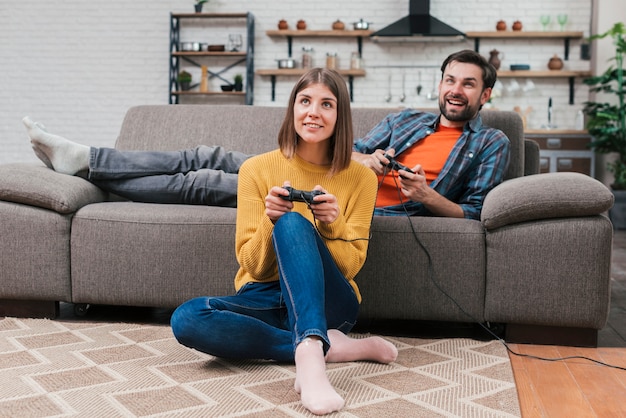 Foto gratuita sonriente joven pareja relajante en casa jugando el videojuego en casa