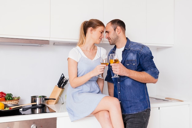 Sonriente joven pareja romántica brindando las copas en la cocina