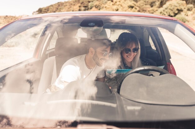 Sonriente joven pareja sentada dentro del coche mirando el mapa