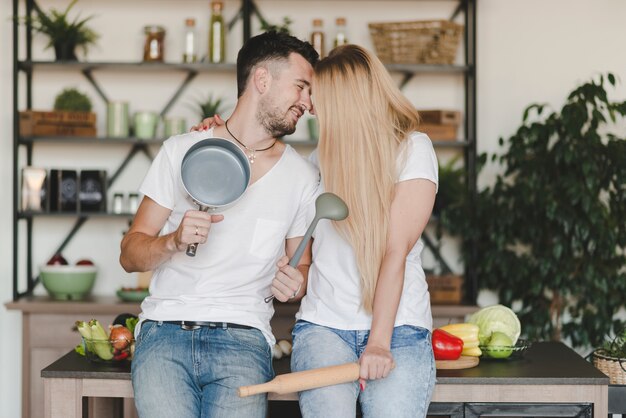 Sonriente joven pareja sentada en el mostrador de la cocina con utensilio