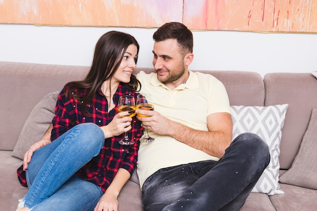 Foto gratuita sonriente joven pareja sentada en el sofá con bebidas en la mano