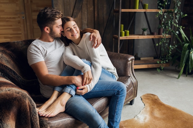 Foto gratuita sonriente joven pareja sentada en el sofá en casa en ropa casual, amor y romance, mujer y hombre abrazándose, vistiendo jeans, pasando tiempo de relax juntos