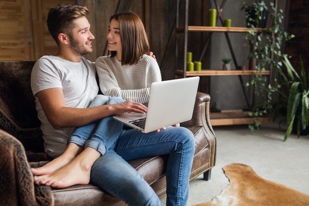 Sonriente joven pareja sentada en el sofá en casa en ropa casual