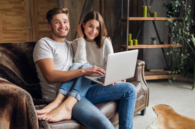 Sonriente joven pareja sentada en el sofá en casa en ropa casual