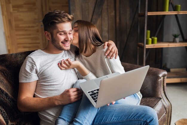 Sonriente joven pareja sentada en el sofá en casa en ropa casual