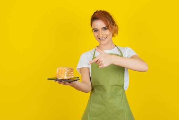 Sonriente joven pelirroja dedo acusador en la rebanada de pastel fresco