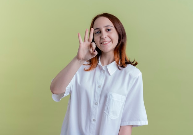 Sonriente joven pelirroja mostrando gesto okey en verde oliva