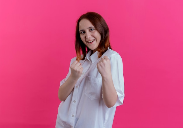 Sonriente joven pelirroja de pie en pose de lucha aislada en rosa