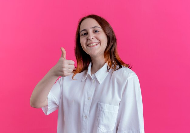 Sonriente joven pelirroja con el pulgar hacia arriba aislado en rosa