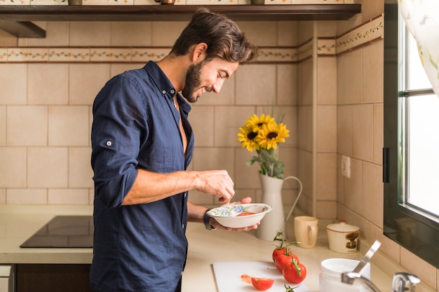 Sonriente joven preparando ensalada en la cocina